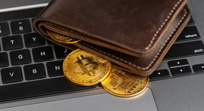 Billetera con monedas de bitcoin sobre una laptop.